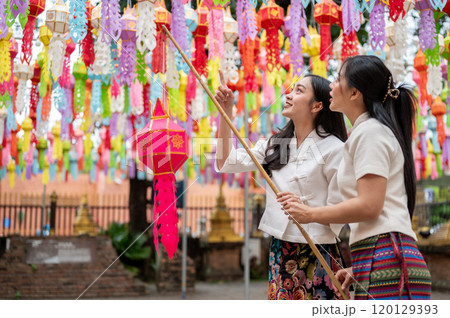Two charming Asian women enjoy hanging a colorful lantern together in a temple. 120129393