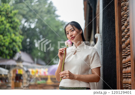 A beautiful Asian woman in a traditional dress stands in a temple, holding a lotus. A beautiful Asian woman in a traditional dress stands in a temple, holding a lotus. 120129401