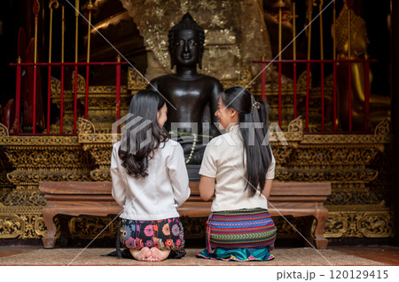 A back view of two beautiful Asian women in traditional dresses sitting in a temple, making wishes. 120129415