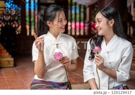 Two charming, smiling Asian women sitting in a temple and enjoying a conversation together. 120129417