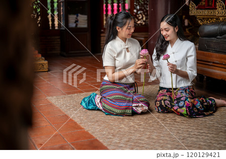 Two charming Asian women sitting in a temple and enjoying folding lotus flowers together. 120129421
