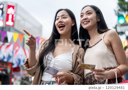 Two cheerful Asian female friends are excited and amazed by the various food stalls at a market. 120129481