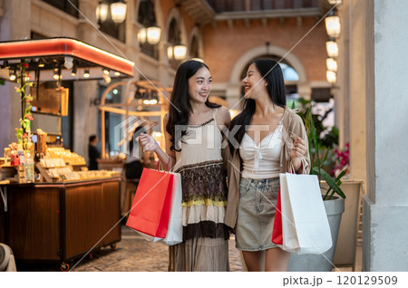 Two attractive Asian women enjoy a shopping spree at a mall, carrying their shopping bags. Two attractive Asian women enjoy a shopping spree at a mall, carrying their shopping bags. 120129509