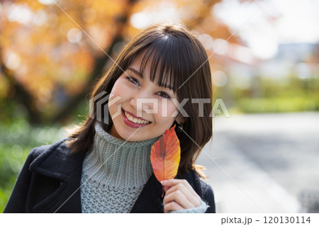 大阪府大阪市都島区の桜之宮公園の紅葉を背景にして左手で葉っぱを持つ笑顔の若い女性 120130114