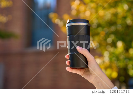 Woman holding reusable coffee cup outdoors in autumn 120131712