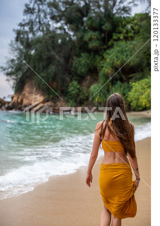 Enjoy a Serene Beach Walk A Woman in a Beautiful Yellow Dress Strolling by the Ocean Shore 120133377