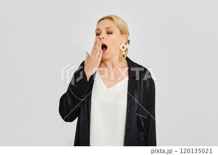 Woman yawning while wearing stylish outfit against neutral background in a calm indoor setting 120135021