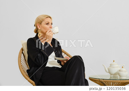 Woman enjoying tea in a minimalist setting while seated on a rattan chair during the day Woman enjoying tea in a minimalist setting while seated on a rattan chair during the day 120135036
