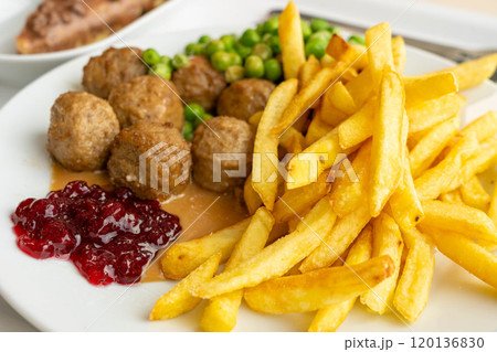 Meatballs with french fries, green peas, bechamel sauce and cranberry jam, meat balls on white plate 120136830
