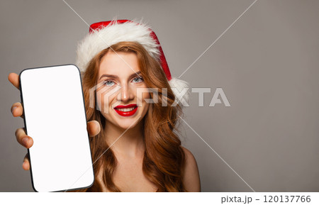 Joyful young smiling woman in red Santa hat showing smartphone  120137766