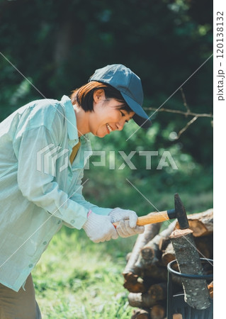 薪割り台に薪を置いてハンマーで叩く女性 薪割り台に薪を置いてハンマーで叩く女性 120138132