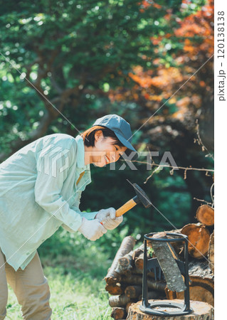 薪割り台に薪を置いてハンマーで叩く女性 薪割り台に薪を置いてハンマーで叩く女性 120138138
