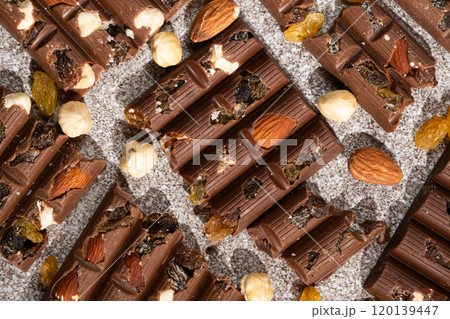 Broken chocolate pieces with nuts and raisins on a stone background top view Broken chocolate pieces with nuts and raisins on a stone background top view 120139447