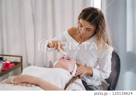 Professional female cosmetologist doing procedure in Cosmetology clinic. Rejuvenation and Hydratation.  120139624