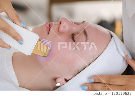 A professional skincare specialist applies a cooling gel on a client's face with a gentle spatula, focusing on precise treatment. A professional skincare specialist applies a cooling gel on a client's face with a gentle spatula, focusing on precise treatment. 120139625