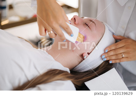 A professional skincare specialist applies a cooling gel on a client's face with a gentle spatula, focusing on precise treatment. 120139629