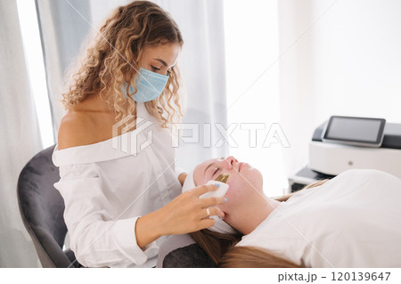 The beautician wearing a protective mask performs a detailed skincare treatment on a client, emphasizing cleanliness and care. 120139647