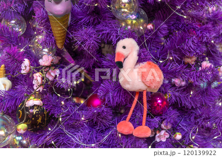Pink flamingo on purple Christmas tree. Soft funny children's toy. Symbol of hope and happiness in new year 120139922