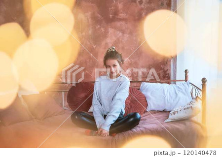 fragile teenage girl in bed hugging pillows surrounded by golden Christmas lights fragile teenage girl in bed hugging pillows surrounded by golden Christmas lights 120140478