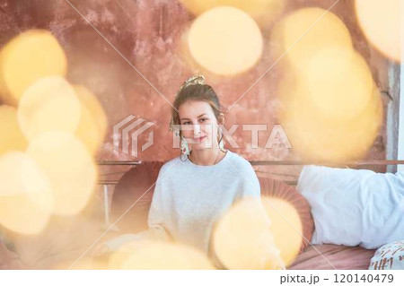fragile teenage girl in bed hugging pillows surrounded by golden Christmas lights 120140479