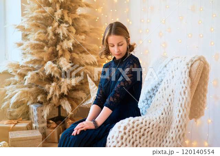 teenage girl in a dress near an unconventional Christmas tree surrounded by golden lights teenage girl in a dress near an unconventional Christmas tree surrounded by golden lights 120140554