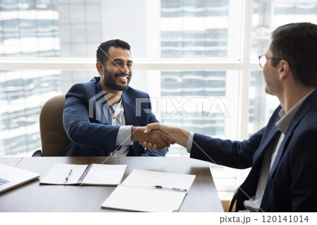 Cheerful young Indian businessman shaking hands with Caucasian business partner Cheerful young Indian businessman shaking hands with Caucasian business partner 120141014