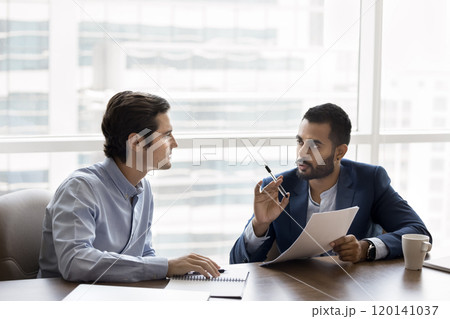 Two diverse serious young male business partners discussing contract terms 120141037