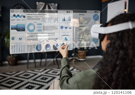 Over-the-shoulder shot of unrecognizable young woman wearing VR headset sitting in living room using app for remote work 120141106