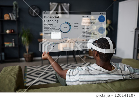 Rear view of unrecognizable young Black man sitting on couch in living room at home using VR headset for work Rear view of unrecognizable young Black man sitting on couch in living room at home using VR headset for work 120141107