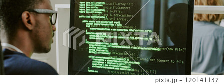 Over shoulder shot of young African American ethical hacker working with code on desktop computer in office, website header 120141137