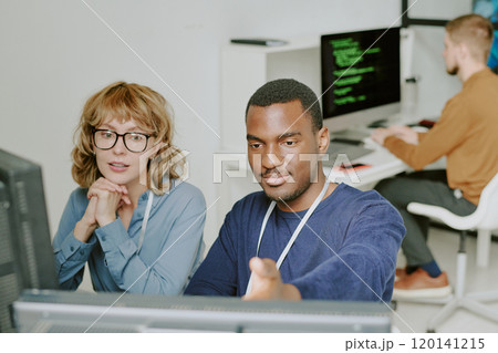 High angle view of young Black man and Caucasian woman looking at desktop computer screen and talking at workplace in IT company office 120141215