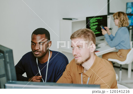 High angle view of two young ethnically diverse programmers working together on new software in modern IT company office 120141216