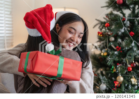 Joyful Young Woman Couple Exchanging Surprise Gift Box by Christmas Tree in Festive Holiday Celebration 120141345
