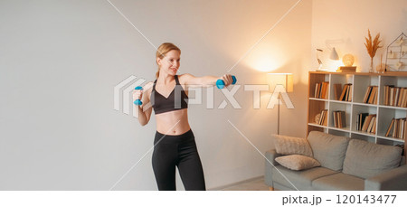 Weight lifting. Muscle stretching. Contented smiling trim girl using dumbbells at home showcasing power and dedication to fitness. Weight lifting. Muscle stretching. Contented smiling trim girl using dumbbells at home showcasing power and dedication to fitness. 120143477