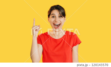 Idea inspiration. Cheerful smiling happy woman in red energetically points up isolated on bright yellow empty space background. Idea inspiration. Cheerful smiling happy woman in red energetically points up isolated on bright yellow empty space background. 120143570