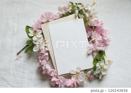 Spring stationery. Pink blossoming Japanese cherry, apple tree branch. Blank paper greeting card, invitation mockup on white linen table background. Feminine wedding styled photo. Flat lay, top view. Spring stationery. Pink blossoming Japanese cherry, apple tree branch. Blank paper greeting card, invitation mockup on white linen table background. Feminine wedding styled photo. Flat lay, top view. 120143656