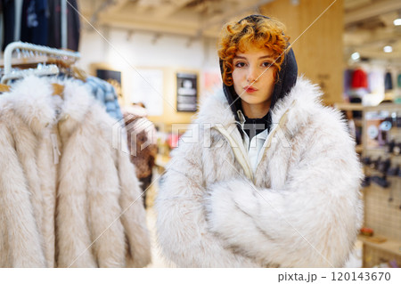 portrait of red-haired attractive young woman trying on fashionable fur coat in store portrait of red-haired attractive young woman trying on fashionable fur coat in store 120143670