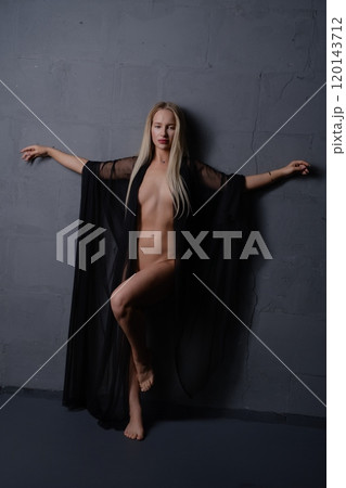 Woman in a dramatic pose wearing a black sheer cape against a gray wall Woman in a dramatic pose wearing a black sheer cape against a gray wall 120143712