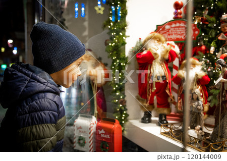 Child looking at festive toy display in Christmas shop window for holiday magic Happy New Year.  120144009