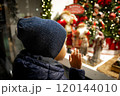 Child in evening in city looks at festive shop window with toys in a Christmas shop window. 120144010