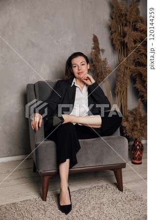 Woman in business suit sitting in chair in gray room 120144259