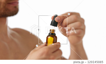 Close-up of man using dropper bottle with serum, representing natural skincare routines for men. 120145085