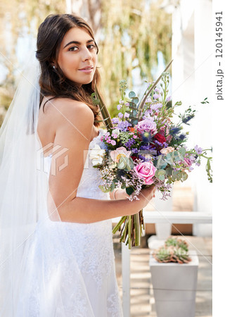 She looks absolutely mesmerizing on her wedding day. Portrait of a happy and beautiful young bride holding a bouquet of flowers while posing outdoors on her wedding day. She looks absolutely mesmerizing on her wedding day. Portrait of a happy and beautiful young bride holding a bouquet of flowers while posing outdoors on her wedding day. 120145941