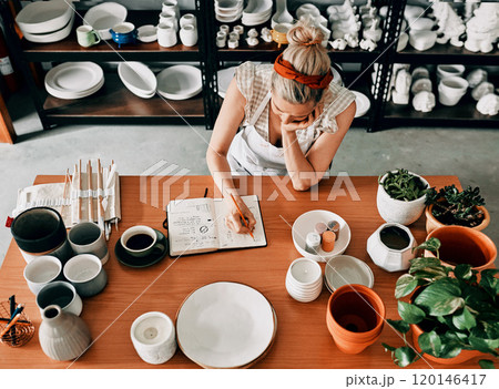 The hard work never ends. High angle shot of an unrecognizable woman sitting and sketching in a notebook in her pottery workshop. The hard work never ends. High angle shot of an unrecognizable woman sitting and sketching in a notebook in her pottery workshop. 120146417