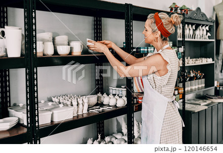 Another addition to the collection. Cropped shot of an attractive mature woman standing and organising her pottery on a shelf in her workshop. Another addition to the collection. Cropped shot of an attractive mature woman standing and organising her pottery on a shelf in her workshop. 120146654