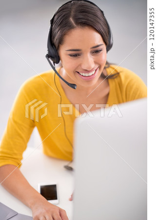 Helping her clients with finesse. Shot of a young customer service representative wearing a headset while sitting by her computer. Helping her clients with finesse. Shot of a young customer service representative wearing a headset while sitting by her computer. 120147355