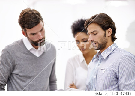 Going over the projects online presence. Shot of three young businesspeople standing in his office and talking over a tablet. 120147433