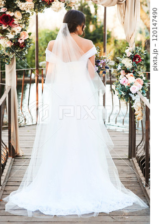 The wait is finally over. Rearview shot a beautiful young bride standing outdoors on her wedding day. 120147490