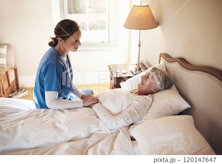 The friendliest face to wake up to. Shot of a young nurse chatting with a senior woman in bed at a retirement home. 120147647