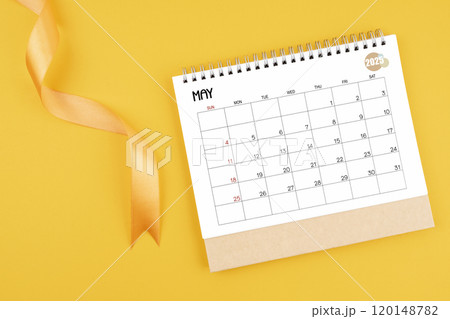 May 2025 desk calendar with yellow ribbon on yellow background. 120148782